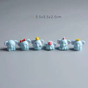 Six cute light-blue mini resin elephant figurines with different accessories (red bow, yellow chick, pink hat, party hat, crown) lined up as car dashboard ornaments