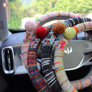 Boho striped fabric steering wheel covers with dachshund patches and fluffy pom poms in pink, cream, black gray and multicolor displayed on car steering wheel
